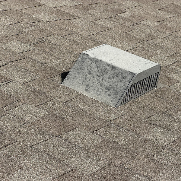 Close up of extreme hail damaged metal box vent on a roof with architectural shingles