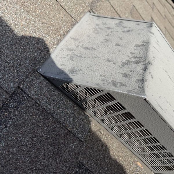 Close up of extreme hail damaged metal box vent on a roof with architectural shingles