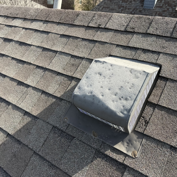Close up of extreme hail damaged metal box vent on a roof with architectural shingles