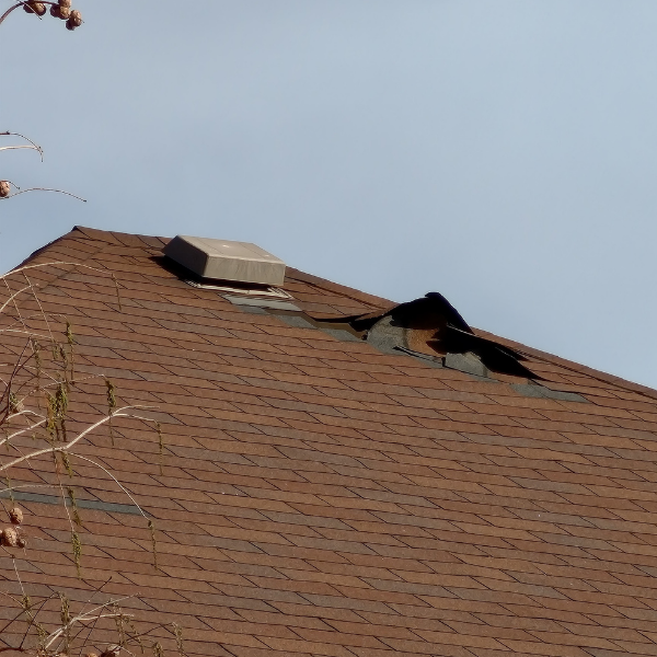 picture of a two-story house showing extreme damage that tore off a section of asphalt shingles.